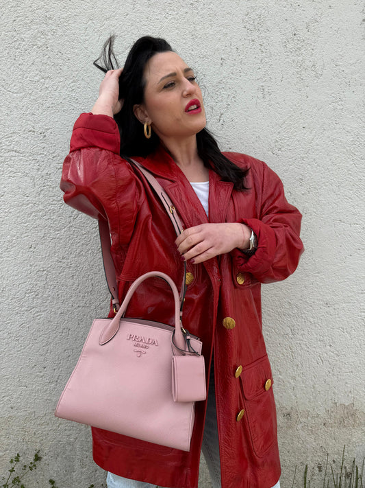 Ragazza che indossa una borsa Prada rosa in pelle saffiano, dotata di un pratico charm con specchietto amovibile, usata, originale, second hand, in ottime condizioni.