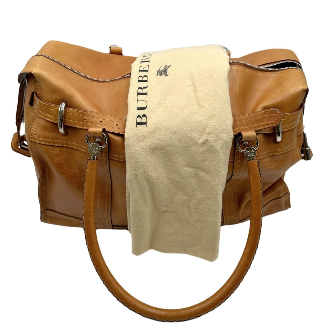 Borsone Burberry in pelle color caramello con parti metalliche argentate, munito di doppi manici stondati. Rifinito con fibbia decorativa sul front. Completo di dustbag. Originale, usato, in condizioni ottime.