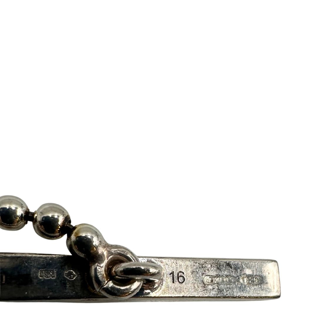 Bracciale Gucci in argento 925 con catena a sfere e pendente con doppia G intrecciata e parzialmente smaltata in nero, attraversata da una barra di chiusura. Completo di sacchetto antipolvere.