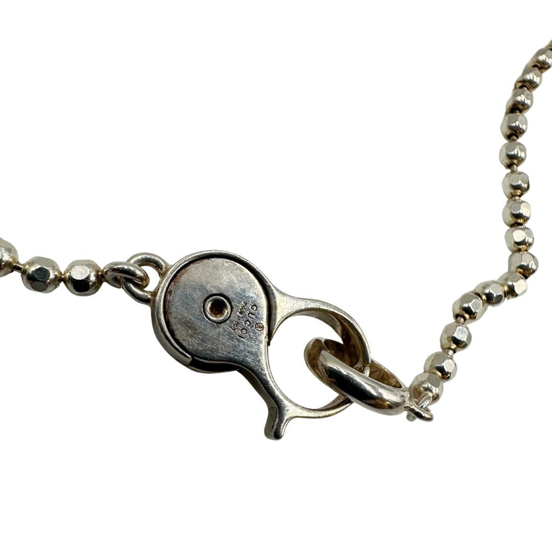 Collana Gucci in argento 925 con catena a sfere sfaccettate pendente a moschettone rotondo che presenta il logo "GG" intrecciato smaltato su fondo marrone/beige. Munita di sacchetto anti polvere e cartellino.