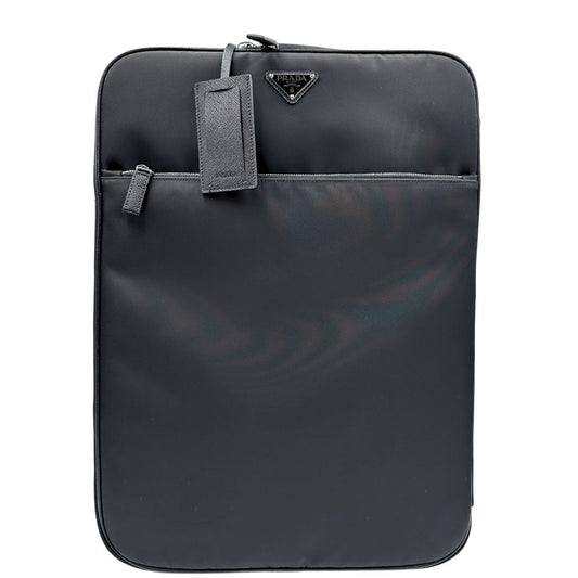 Front di una valigia Prada in tessuto e pelle saffiano nera con dettagli metallici argentati. L’interno è foderato in tessuto jacquard con motivo logo Prada, dotato di cinghie regolabili per fissare il contenuto e tasca con zip. Dispone di doppia chiusura con cerniera e lucchetto numerico in metallo argentato, manico superiore e laterale in pelle, maniglia estraibile e ruote posteriori per facilitarne il trasporto. Completa di dustbag, clochette porta address e card d'autenticità.
