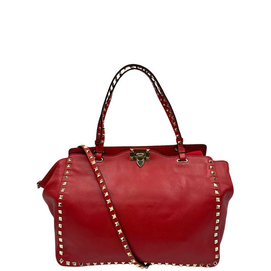 Front di una borsa Valentino Garavani in pelle rossa con parti metalliche dorate; impreziosita da borchie piramidali e munita di doppi manici e tracolla amovibile. Completa di dustbag.