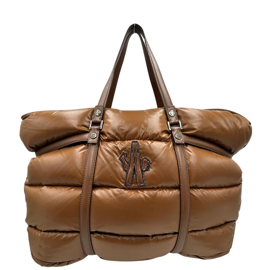 Front di una borsa Moncler in poliuretano color caramello effetto imbottito e finiture in pelle tono su tono, con metalleria dorata. Munita di cartellino. Da indossare a spalla.