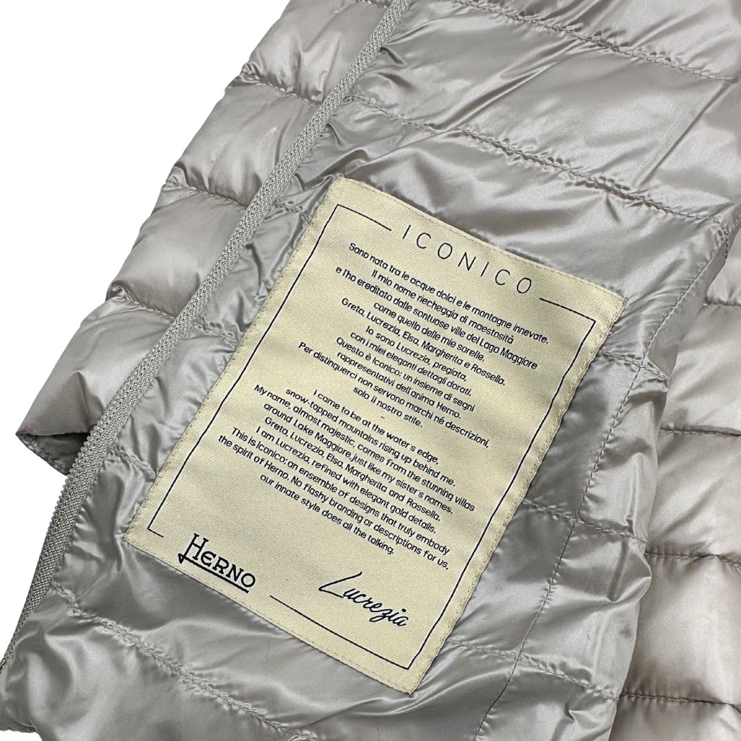 Piumino Herno in 100% poliammide color champagne. Maniche a 3/4 e parti metalliche dorate.