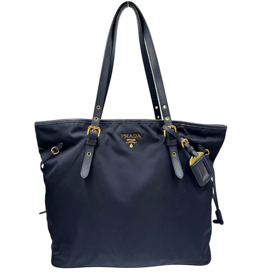 Front di una borsa Prada in nylon blu navy e finiture in pelle saffiano tono su tono, con parti metalliche dorate; munita di un accessorio porta address e doppi manici leggermente regolabili. Indossabile a spalla. Completa di dustbag e card d'autenticità.