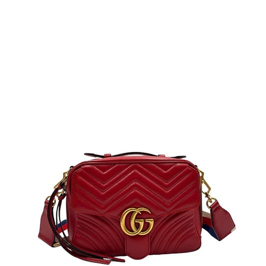 Front di una borsa Gucci Marmont in pelle matelassè rossa e parti metalliche dorate; munita di un manico superiore e di una tracolla in tessuto web blu/bianco/rosso, regolabile ed amovibile. Indossabile a mano o a tracolla. Completa di dustbag.