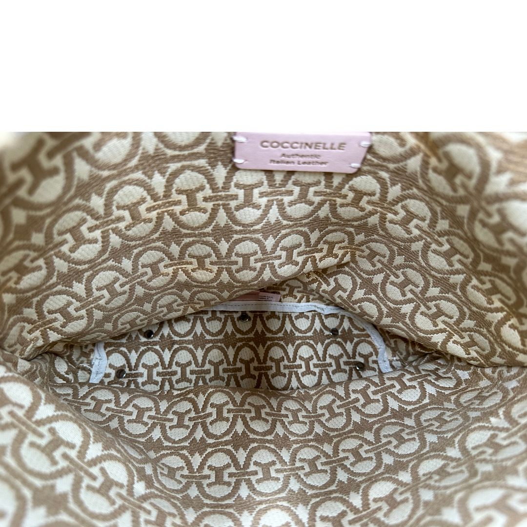 Interno di una borsa Coccinelle in pelle color cammello con parti metalliche argentate e interno in tessuto logato; munita di un manico singolo leggermente regolabile. Indossabile a spalla.