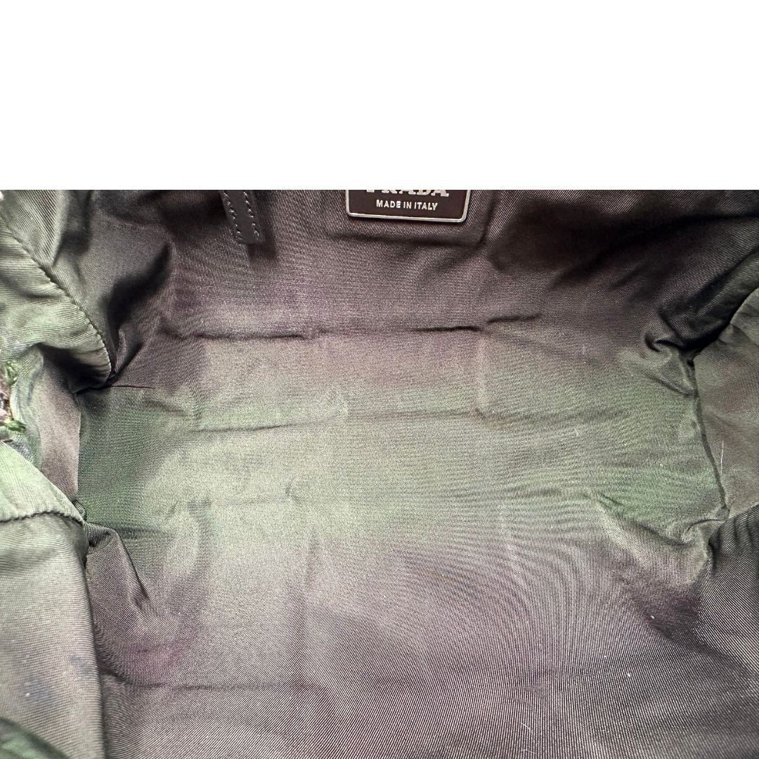 Interno di un bauletto Prada in tessuto nylon verde militare e pelle marrone, con dettagli metallici argentati, indossabile a mano.