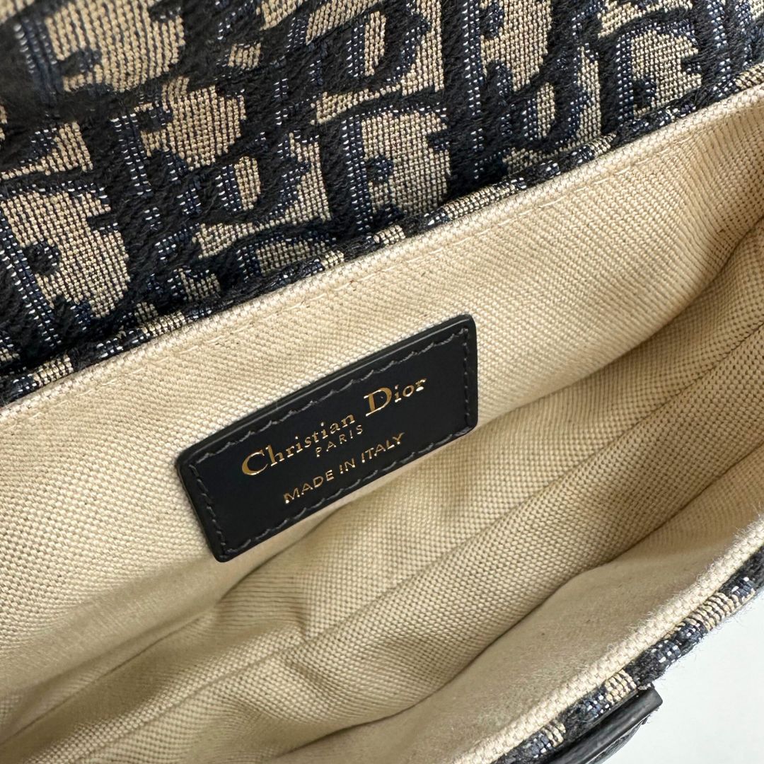 Interno Borsa Saddle Dior in tessuto beige con trama Dior Oblique nera e blu, finiture in pelle blu notte e parti metalliche dorate. Munita di manico singolo e tracolla regolabile, e amovibile. Completa di corredo. Originale, usato, condizioni ottime.