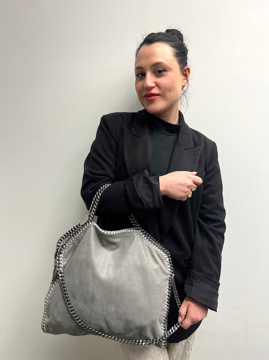 Ragazza che indossa una borsa Stella McCartney Falabella in tessuto vegano grigia rifinita con catene in metallo argentato. Completa di dustbag.