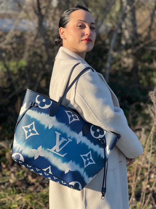 Ragazza che indossa una borsa Louis Vuitton Neverfull MM in canvas base tie-dye nelle tonalità del blu e bianco, con finiture in pelle blu navy. Da un lato ha stampa Monogram Giant, dall'altra Monogram. Parti metalliche argentate; munita di doppi manici e dustbag, indossabile a spalla.