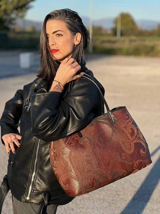 Ragazza che indossa una borsa Etro in canvas trama paisley bordeaux e parti in pelle nere, munita di doppi manici. Indossabile a spalla.