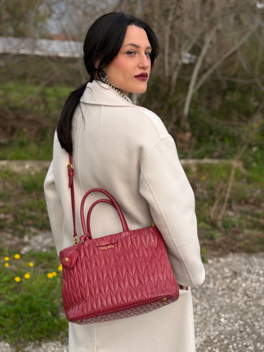 Ragazza che indossa una borsa Miu Miu in pelle matelassé rosa con parti metalliche dorate, usata, originale, second hand, in ottime condizioni.