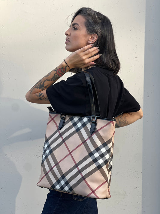 Ragazza che indossa una borsa tote Burberry in canvas trama tartan, finiture in pelle lucida nere e parti metalliche effetto renio.