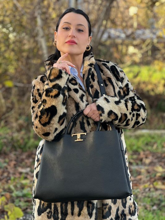 Ragazza che indossa una borsa Tod's in pelle nera martellata, con parti metalliche dorate; munita di manici stondati e di una tracolla regolabile ed amovibile. Completa di dustbag.