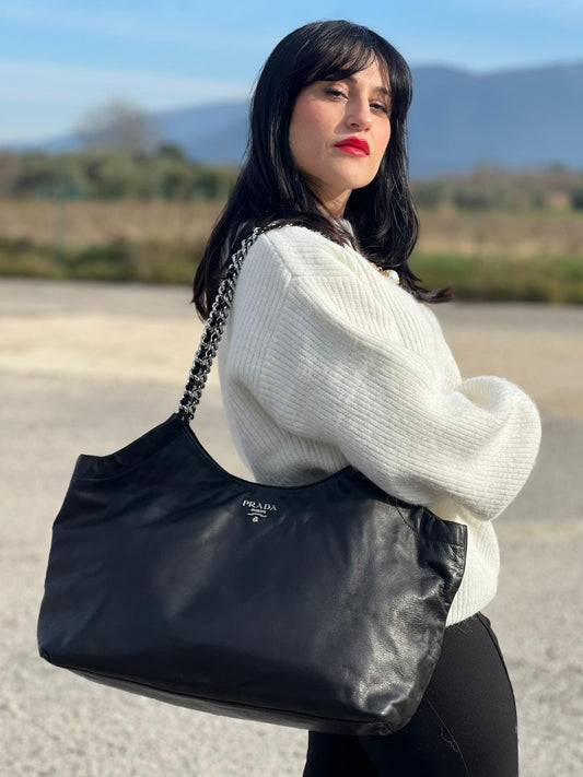 indossata della Borsa Prada in pelle nera con parti metalliche argentate; munita di doppi manici in pelle e catena intrecciati, da portare a spalla, di lusso, originale, ottime condizioni, usata.