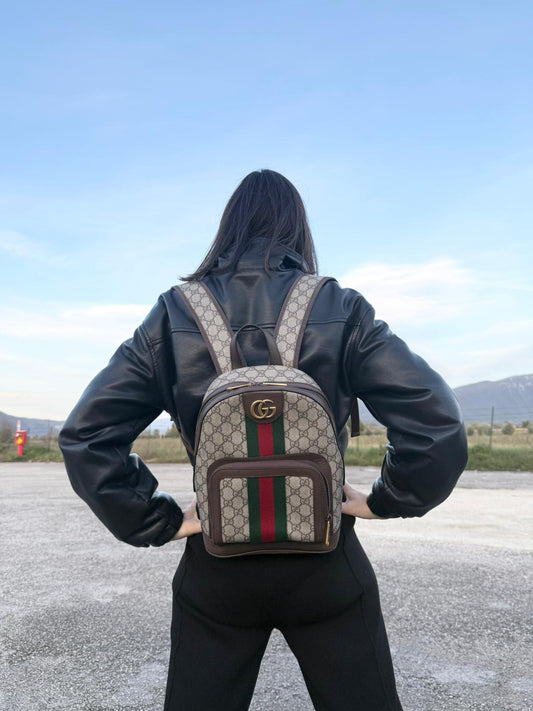 Ragazza che indossa uno zaino Gucci in canvas beige GG con finiture in pelle marroni e parti metalliche dorate. Iconica striscia Web in verde/rosso sul front, con cinghie regolabili. Full set.