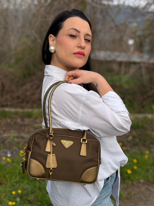 Ragazza che indossa un bauletto Prada in tessuto nylon e pelle saffiano bronzo, con dettagli metallici dorati, indossabile a spalla, usato, originale, second hand, in ottime condizioni.