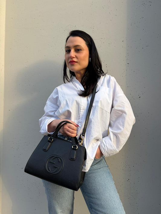 Ragazza che indossa una borsa Gucci in pelle martellata nera, con parti metalliche dorate, indossabile a mano o a tracolla, usata, originale, second hand, in ottime condizioni.