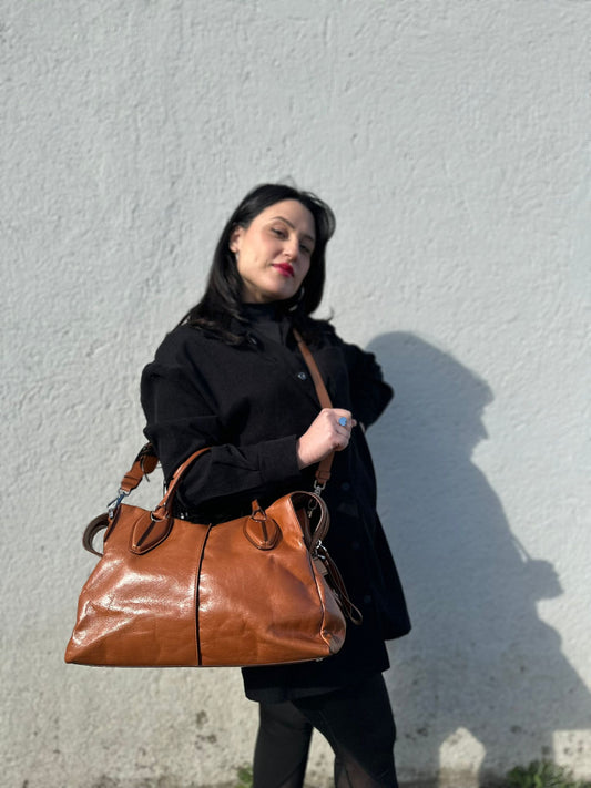 Ragazza che indossa un bauletto Tod's in pelle color cognac con parti metalliche argentate, munito di doppi manici stondati e una tracolla amovibile e regolabile. Completo di dustbag.