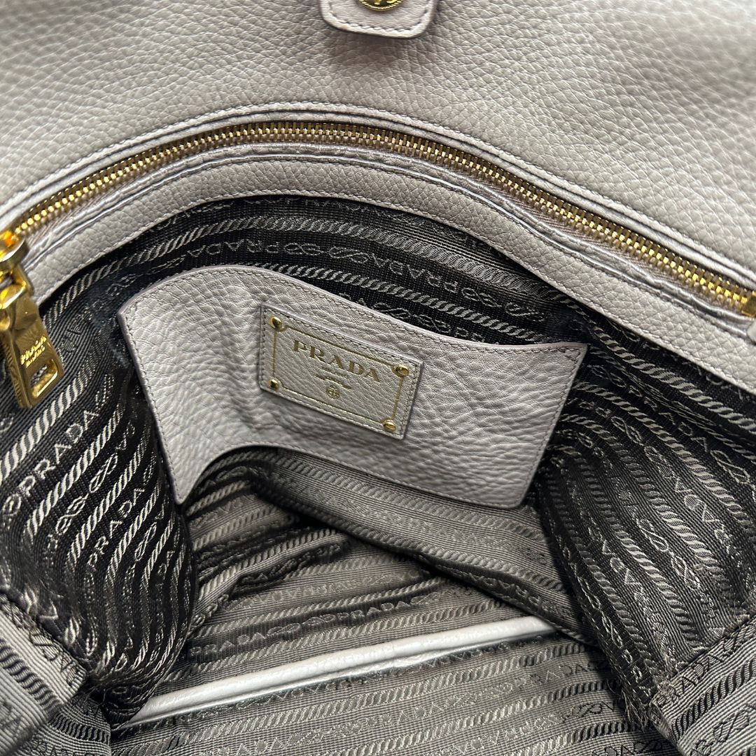 interno Borsa Prada in pelle grigia martellata con parti metalliche dorate; munita di cerniere laterali e doppi manici, indossabile a spalla, di lusso, originale, ottime condizioni, usata.