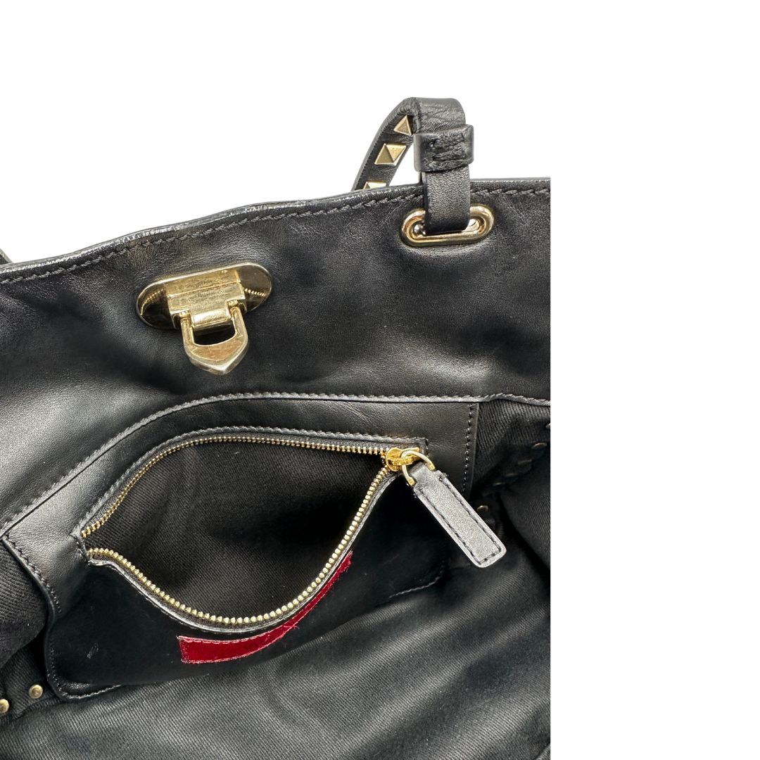 Tasca interna di una Borsa Valentino Garavani in pelle nera con parti metalliche dorate; impreziosita da borchie piramidali e munita di doppi manici e una tracolla amovibile. Completa di dustbag e cartellino. Originale, usata, di lusso, in ottime condizioni.