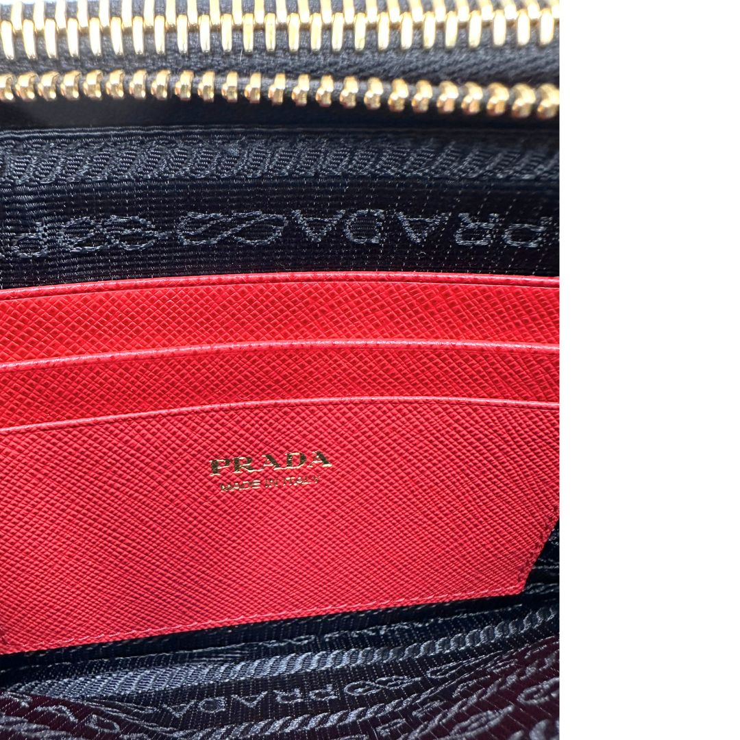 Interno, Prada WOC in pelle saffiano nera decorata con una vivace stampa a cuori rossi. indossabile a tracolla oppure a mano. Originale, usata, di lusso, in ottime condizioni.