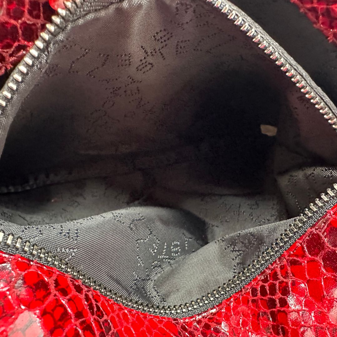 Interno, Borsa Stella McCartney, modello compatto e grintoso, realizzata in ecopelle effetto pitone rosso lucido e impreziosita da dettagli con catena metallica nera lungo i bordi. Indossabile a tracolla. Originale, usata, di lusso, in ottime condizioni.
