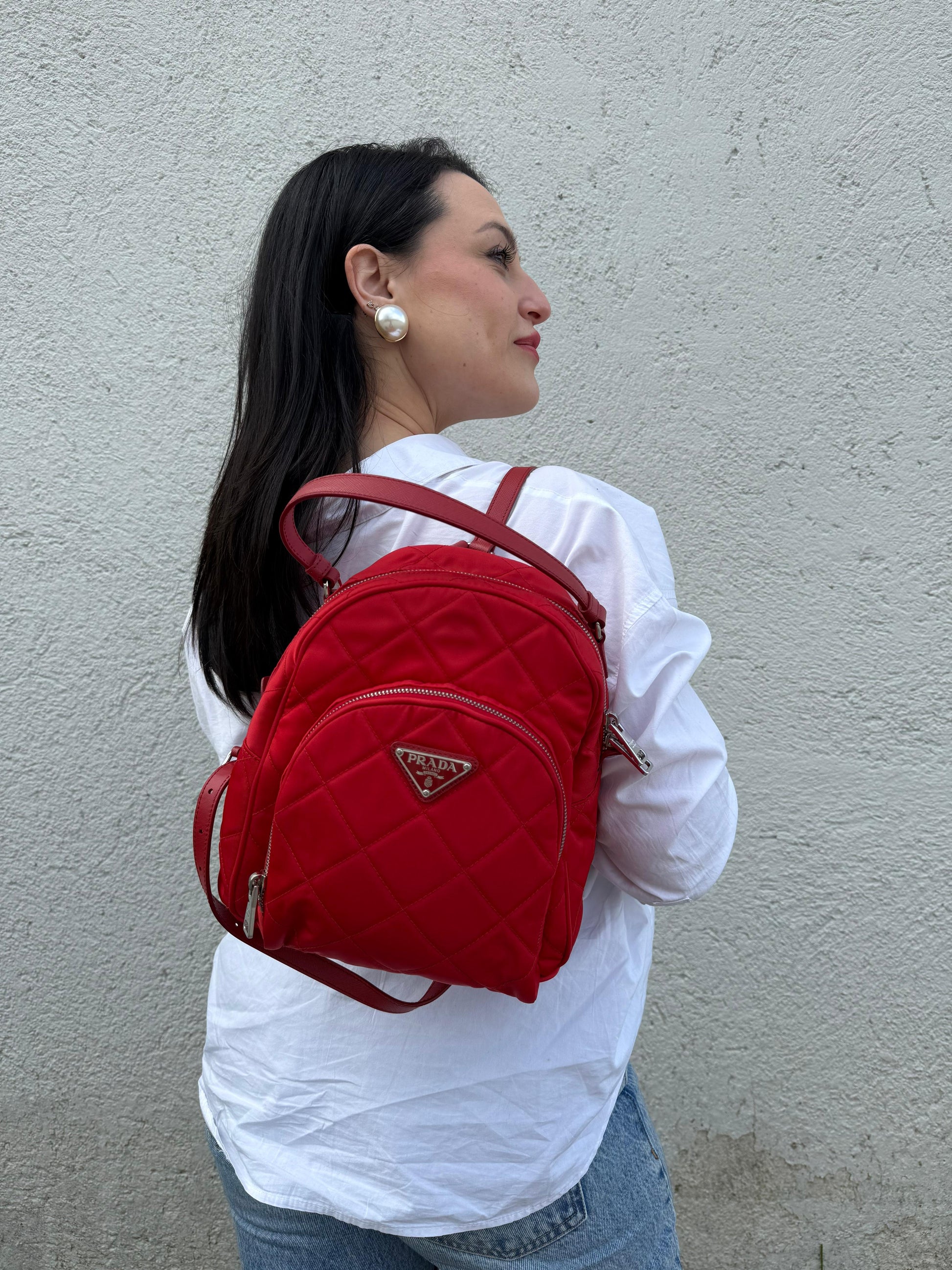 Ragazza che indossa uno zaino Prada in tessuto sintetico rosso e finiture in pelle tono su tono, usato, originale, second hand, in ottime condizioni.