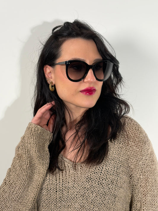 Ragazza che indossa un paio di occhiali da sole Bottega Veneta in acetato nero con lenti sfumate grigie, usati, originali, second hand, in ottime condizioni.