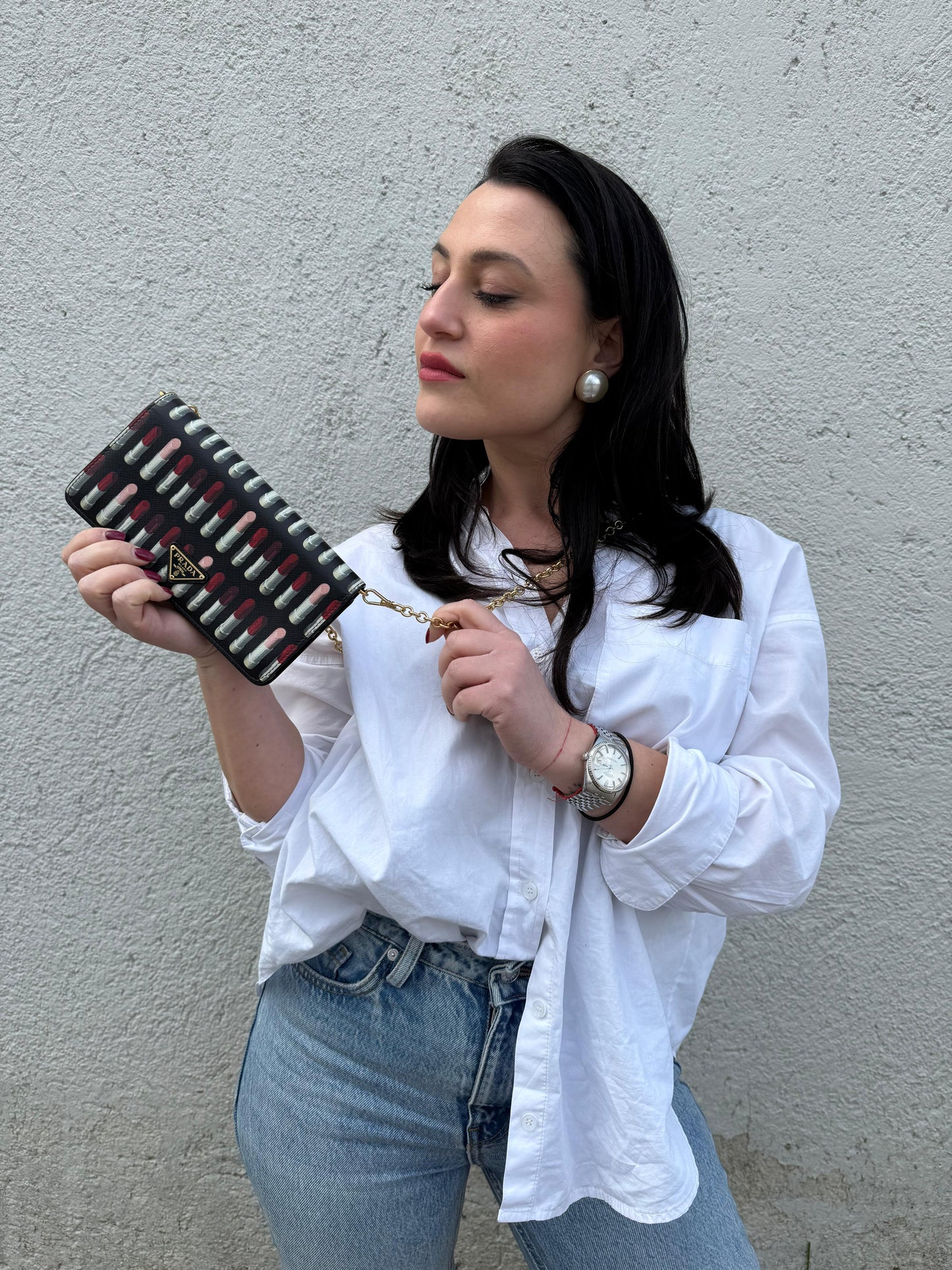 Ragazza che indossa un Prada WOC in pelle saffiano nera, decorato con una vivace stampa di rossetti. Indossabile a tracolla oppure a mano, usato, originale, second hand, in ottime condizioni.