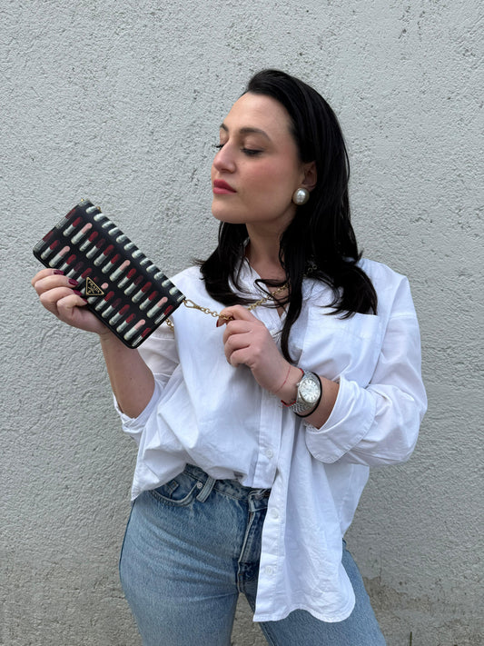 Ragazza che indossa un Prada WOC in pelle saffiano nera, decorato con una vivace stampa di rossetti. Indossabile a tracolla oppure a mano, usato, originale, second hand, in ottime condizioni.