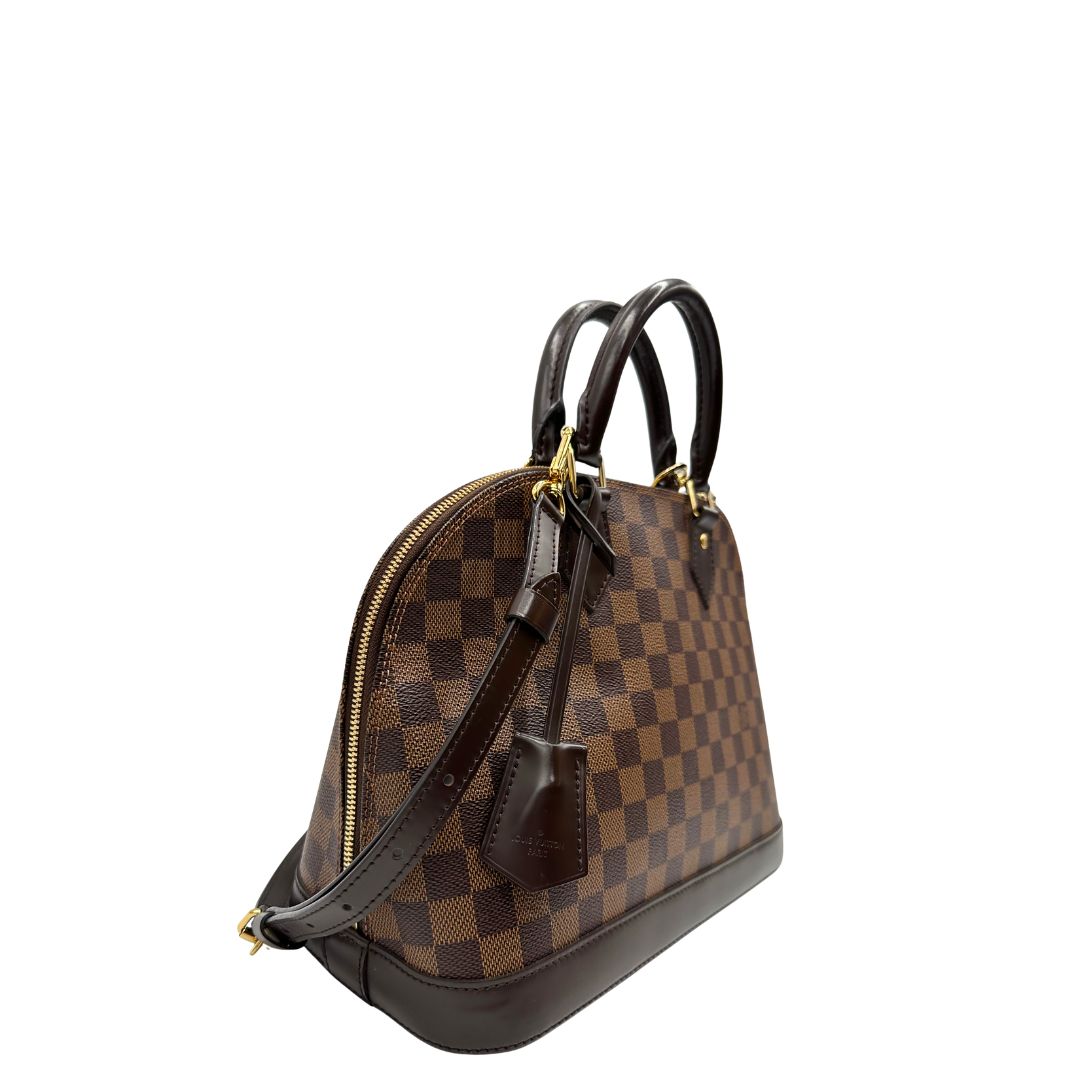 Lato destro, Strutturata borsa Alma PM LV in canvas Damier Ébène e hardware dorato, indossabile a mano oppure a tracolla.
