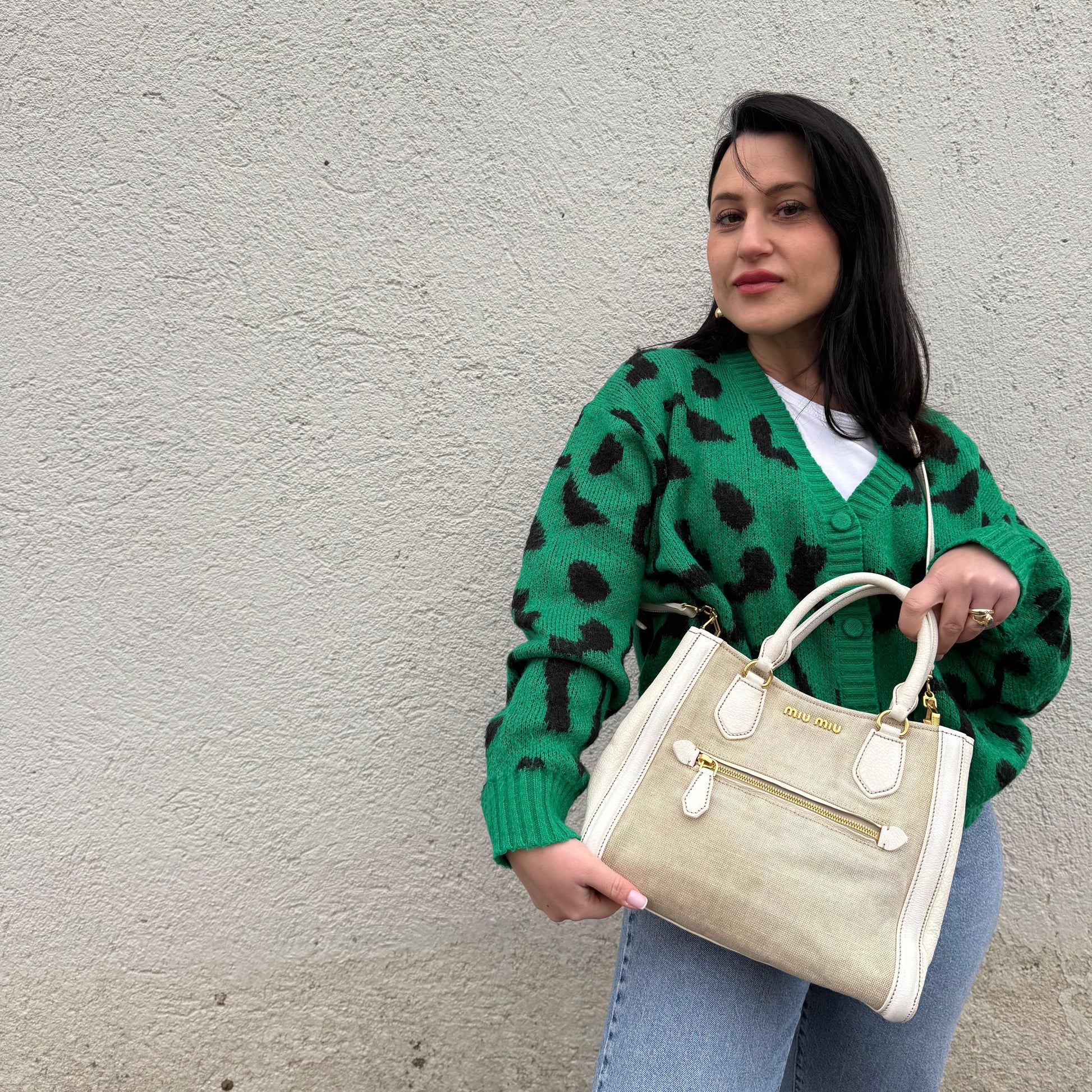 Ragazza che indossa una borsa Miu Miu in misto lino avorio con finiture in pelle color bianco latte e parti metalliche dorate; munita di doppi manici stondati ed una tracolla amovibile e regolabile. Completa di card d'autenticità. Indossabile a mano e a tracolla.