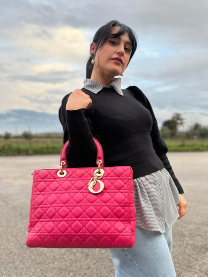 Ragazza che indossa una borsa Lady Dior Large in pelle fucsia in trama cannage. Doppi manici rigidi, con parti metalliche dorate. Completa di dustbag. Indossabile a mano.