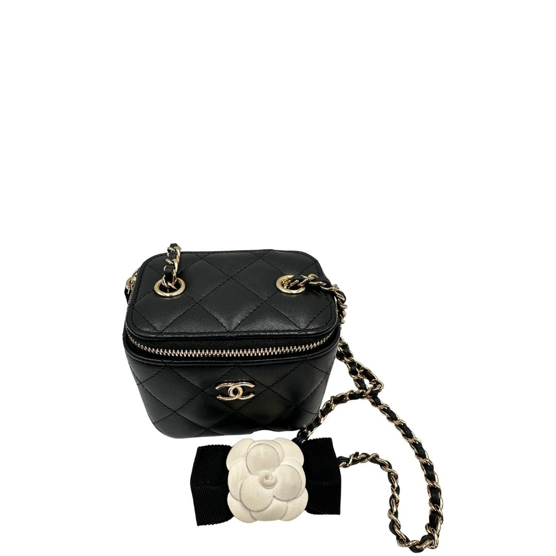 Vista dall'alto di una borsa Chanel in pelle matelassè nera rifinita con parti metalliche dorate; munita di una tracolla in pelle e catena intrecciata decorata con fiocco e camelia. Completa di scatola logata.