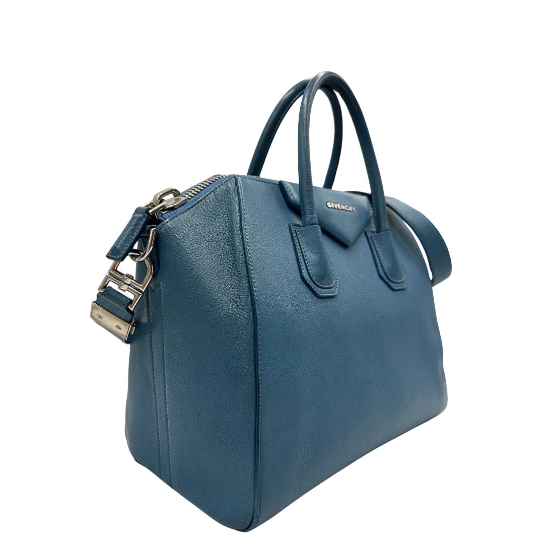 Borsa Givenchy Antigona in pelle martellata blu petrolio munita di doppi manici stondati e tracolla. Parti metalliche argentate. Completa di dustbag. Originale, usato, in condizioni ottime. 