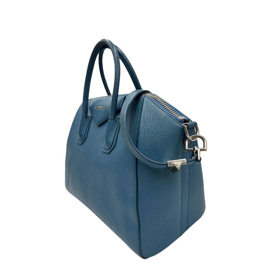 Borsa Givenchy Antigona in pelle martellata blu petrolio munita di doppi manici stondati e tracolla. Parti metalliche argentate. Completa di dustbag. Originale, usato, in condizioni ottime. 
