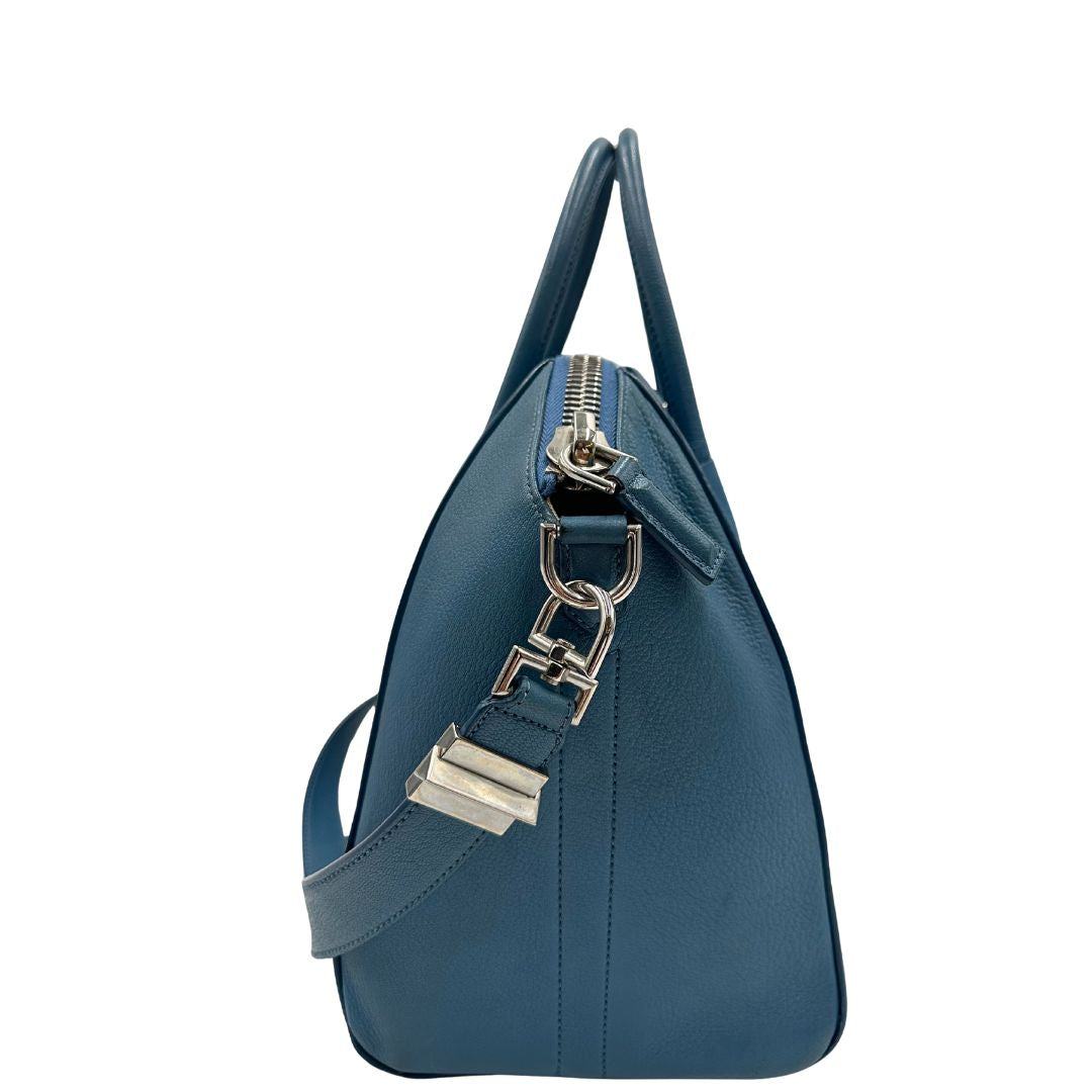 Borsa Givenchy Antigona in pelle martellata blu petrolio munita di doppi manici stondati e tracolla. Parti metalliche argentate. Completa di dustbag. Originale, usato, in condizioni ottime. 