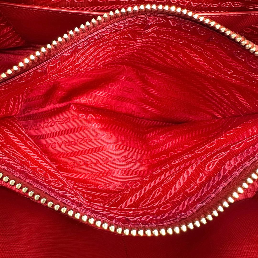 interno Borsa in pelle saffiano rossa con parti metalliche dorate; munita di doppi manici stondati e una tracolla amovibile e regolabile. 