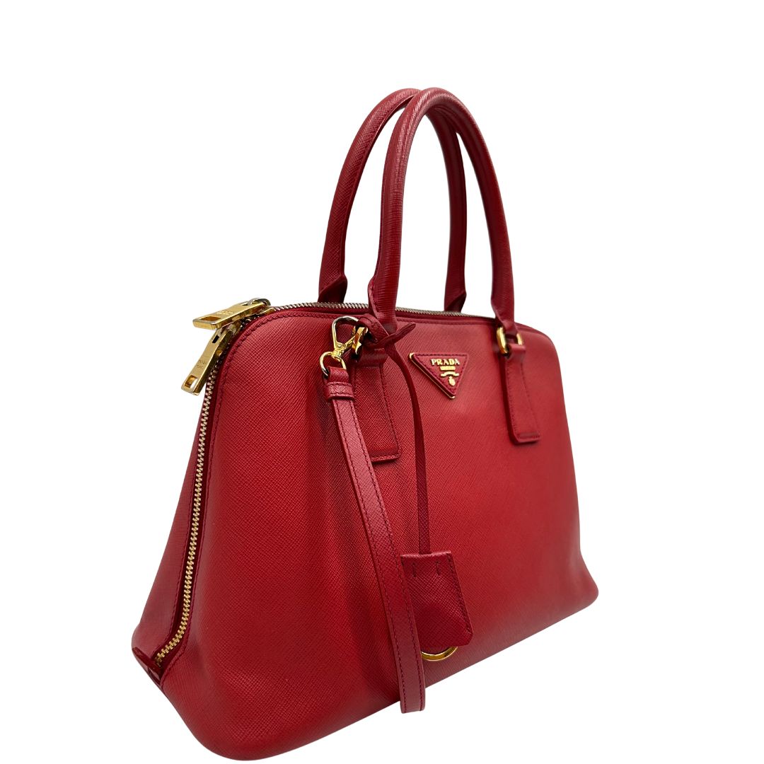 lato Borsa in pelle saffiano rossa con parti metalliche dorate; munita di doppi manici stondati e una tracolla amovibile e regolabile. 