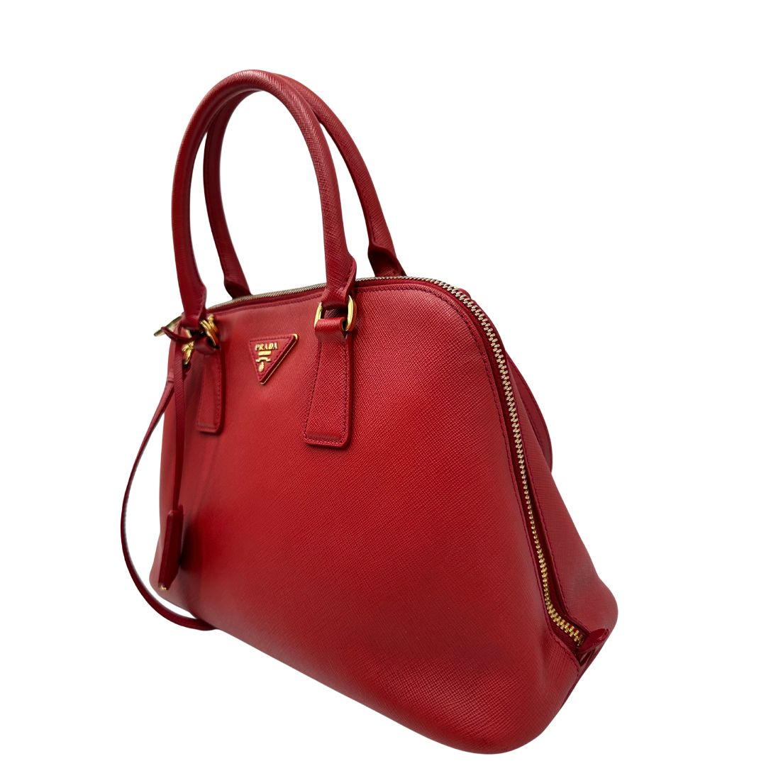 lato Borsa in pelle saffiano rossa con parti metalliche dorate; munita di doppi manici stondati e una tracolla amovibile e regolabile. 