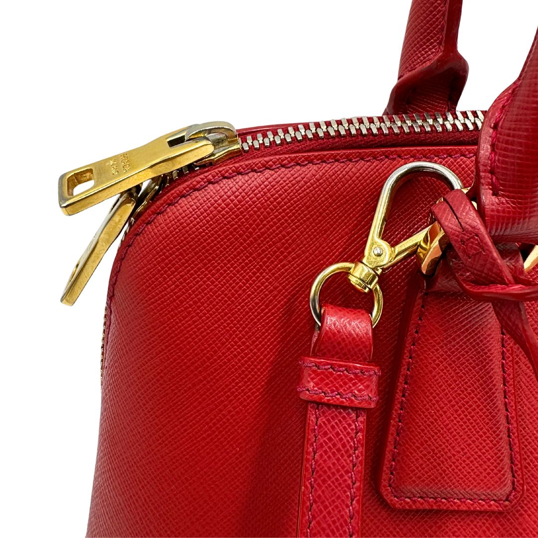 angolo  Borsa in pelle saffiano rossa con parti metalliche dorate; munita di doppi manici stondati e una tracolla amovibile e regolabile. 