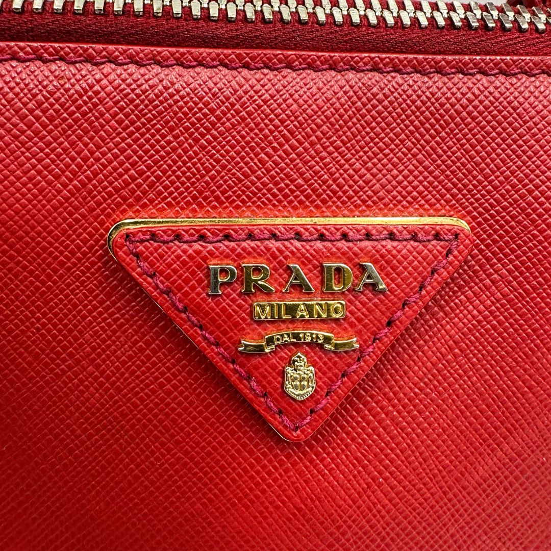 logo Borsa in pelle saffiano rossa con parti metalliche dorate; munita di doppi manici stondati e una tracolla amovibile e regolabile. 