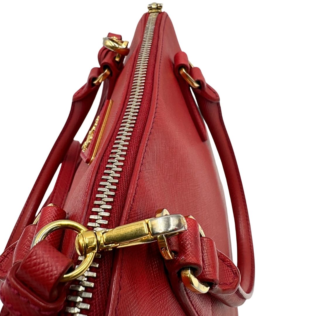 cerniera Borsa in pelle saffiano rossa con parti metalliche dorate; munita di doppi manici stondati e una tracolla amovibile e regolabile. 