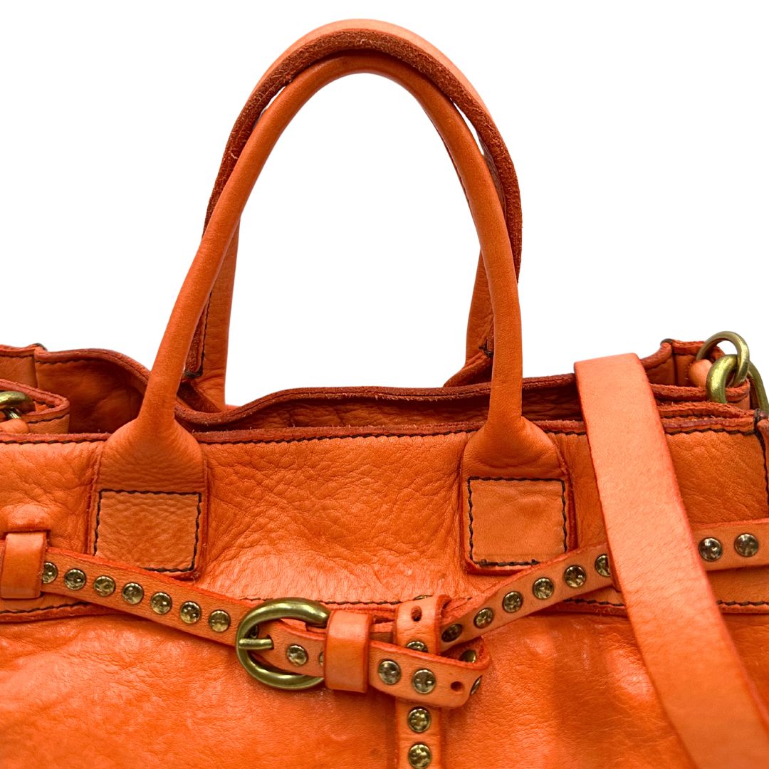 Manici di una satchel Campomaggi in pelle arancione; munita di doppi manici e tracolla amovibile e regolabile. Parti metalliche dorate. Completa di dustbag e crema idratante per pelli.