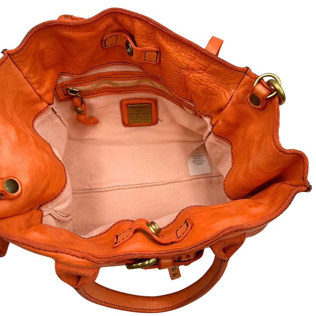 Interno di una satchel Campomaggi in pelle arancione; munita di doppi manici e tracolla amovibile e regolabile. Parti metalliche dorate. Completa di dustbag e crema idratante per pelli.