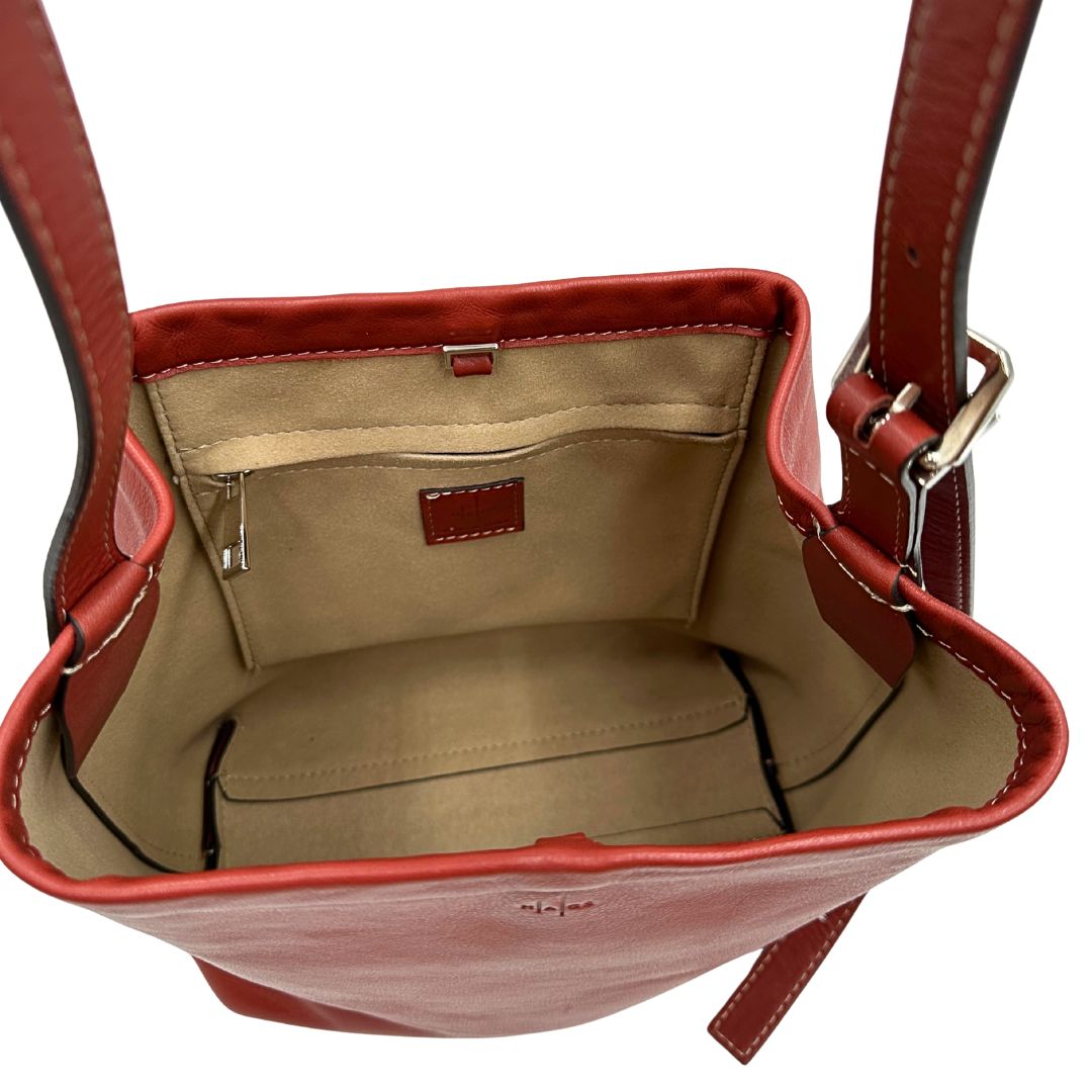 Interno di una borsa a secchiello Hags in pelle color marrone bruciato con manico regolabile. Parti metalliche argentate. Indossabile a spalla o a tracolla. Completa di dustbag.