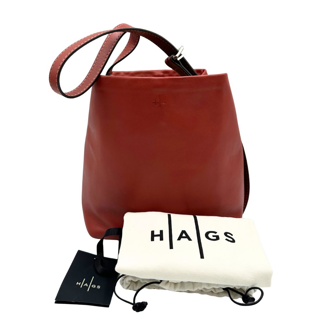 Borsa a secchiello Hags in pelle color marrone bruciato con manico regolabile. Parti metalliche argentate. Indossabile a spalla o a tracolla. Completa di dustbag.