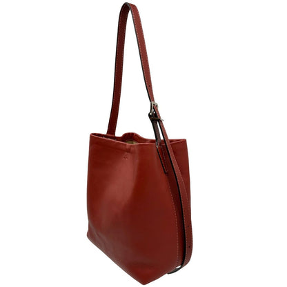 Laterale destro di una borsa a secchiello Hags in pelle color marrone bruciato con manico regolabile. Parti metalliche argentate. Indossabile a spalla o a tracolla. Completa di dustbag.